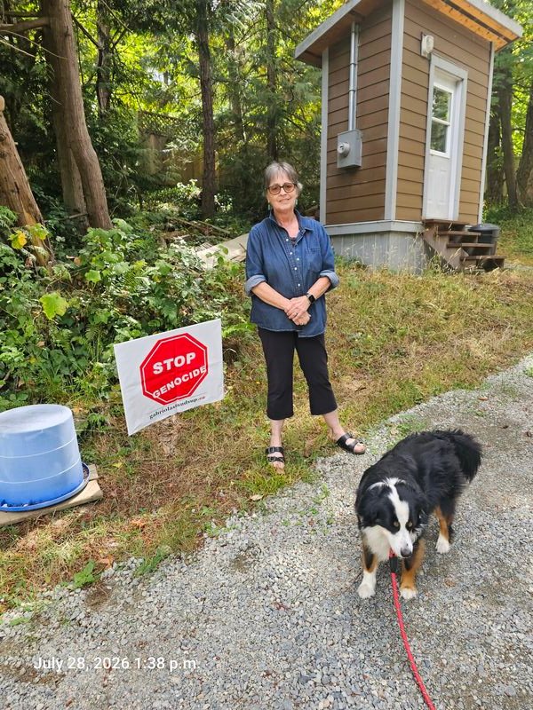 Lynn with her Stop Genocide sign and dog on Norwich Road, Gabriola