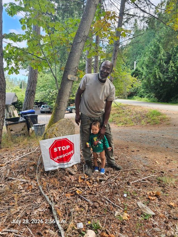 Richard with a child, and their Stop Genocide sign on Pequod Crescent, Gabriola