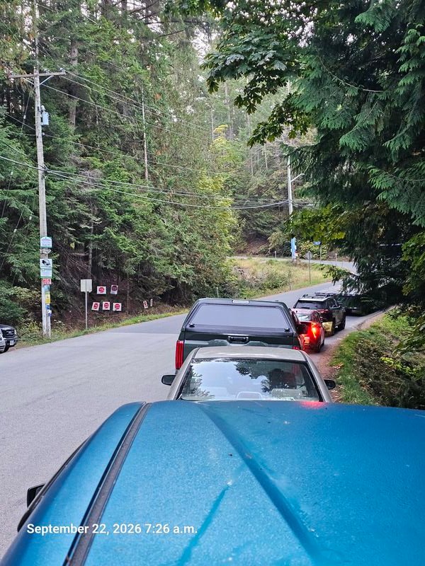 Cars lined up for the ferry passing Stop Genocide signs on Taylor Bay Road, Gabriola - signs #123-#130